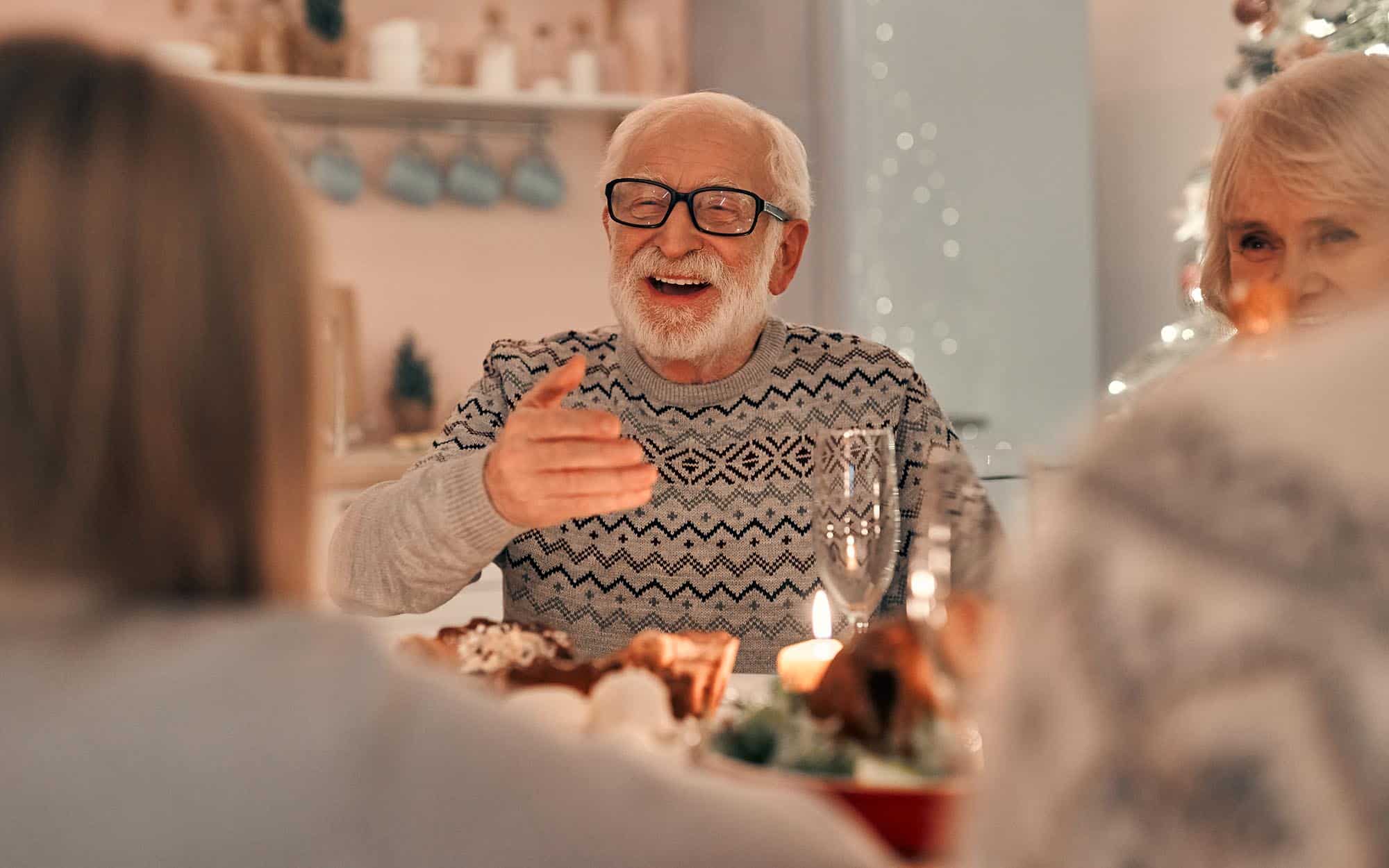 Front view of a senior man sitting at the table surrounded by family on the holidays