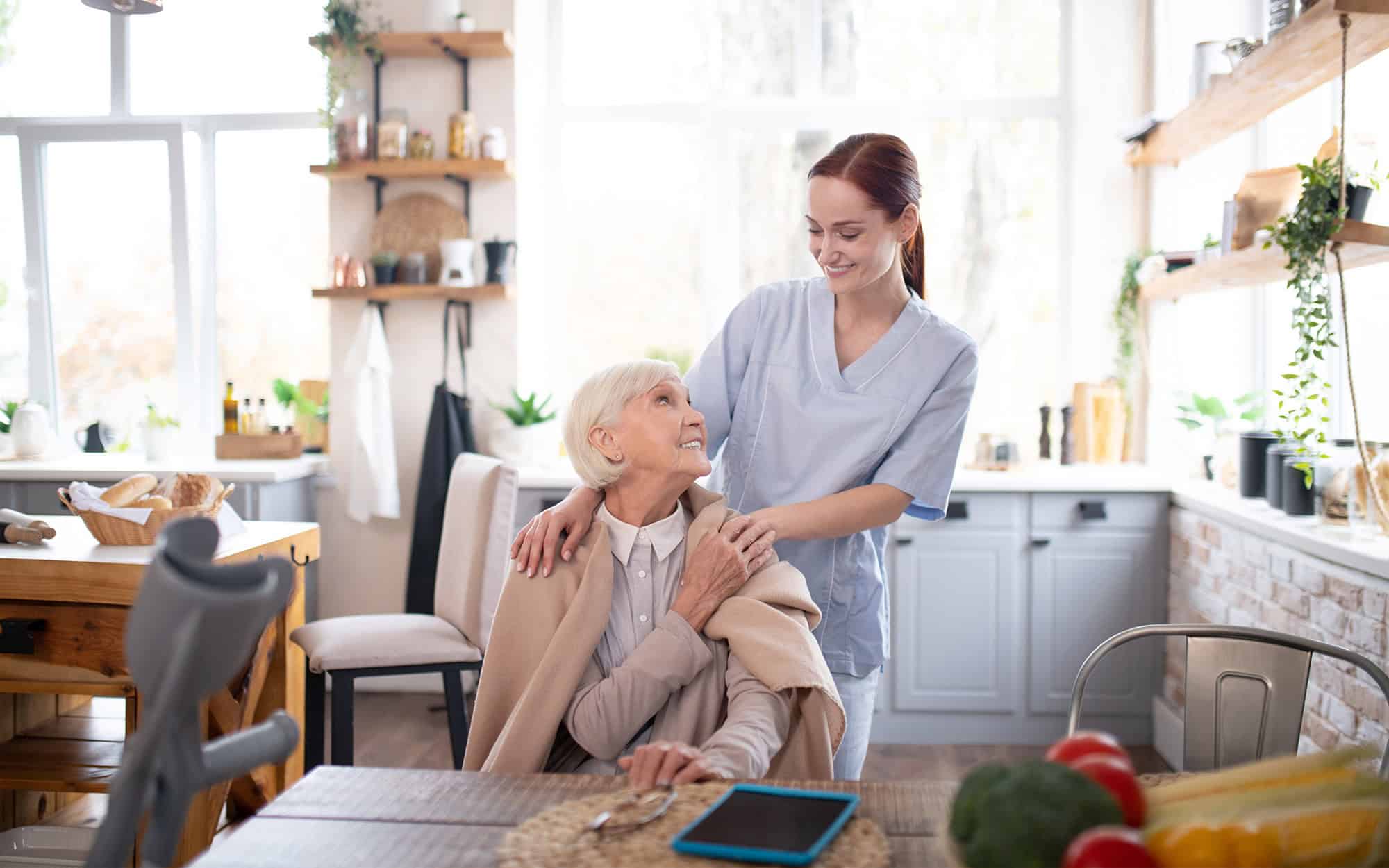 Front view of an elder sitting down and smiling up at her caregiver